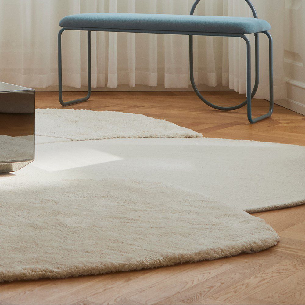 Natural lighting, cropped perspective view of a rug topped with a glass table next to a bench.