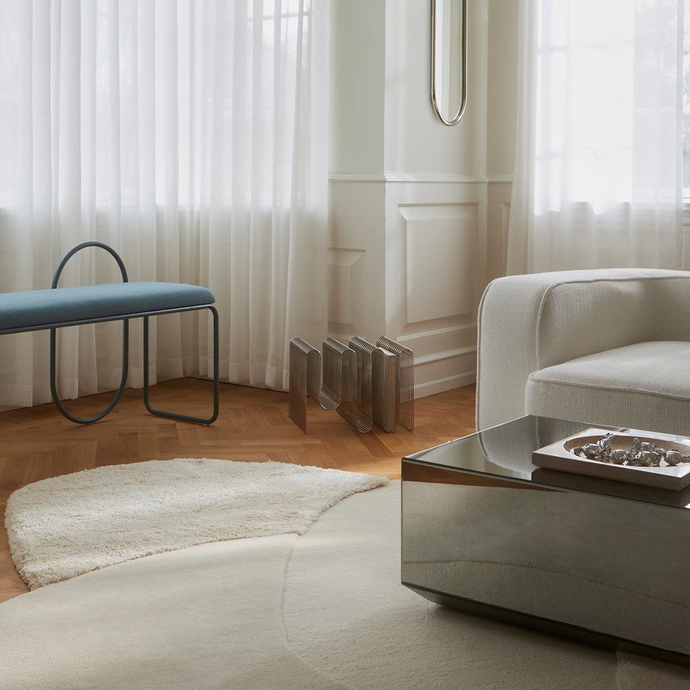 Sunlit living room with a bench, sofa, and mirror table placed in a wide rug.