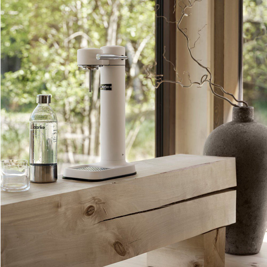 A counter with an empty cylindrical shaped carbonator placed next to a carbonated drink in a bottle.