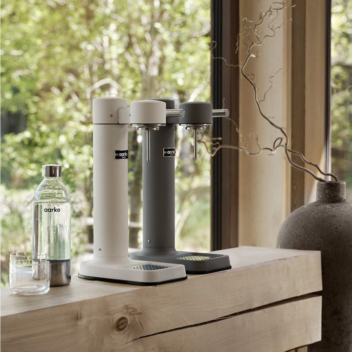 A counter with 2 empty cylindrical shaped carbonators placed next to a carbonated drink in a bottle.