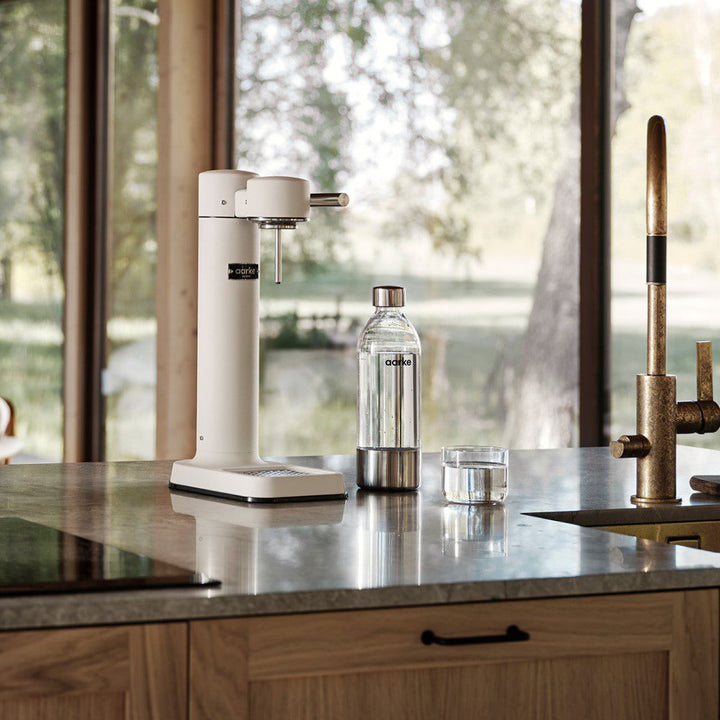 A kitchen counter with a cylindrical shaped carbonator placed next to a carbonated drink in a bottle.