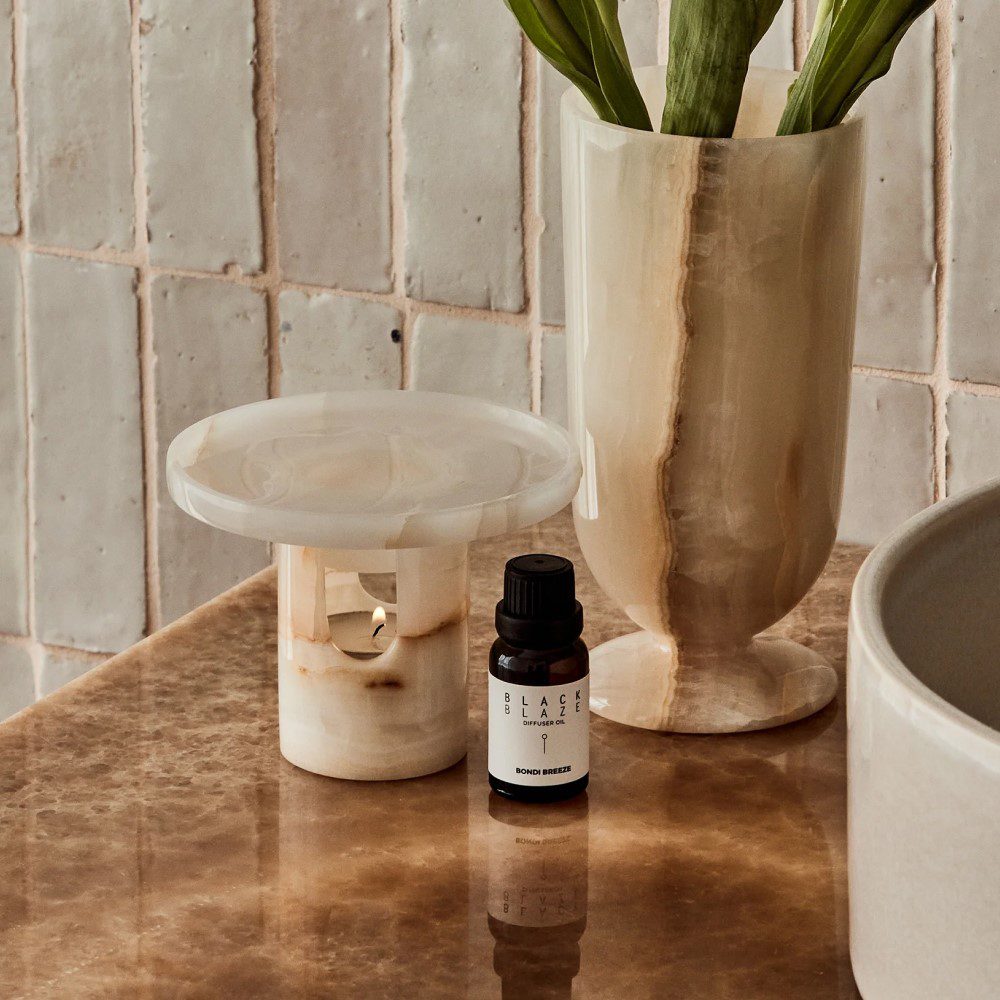 A cylinder-shaped oil diffuser with a round tray on top placed next to an oil bottle and a vase.