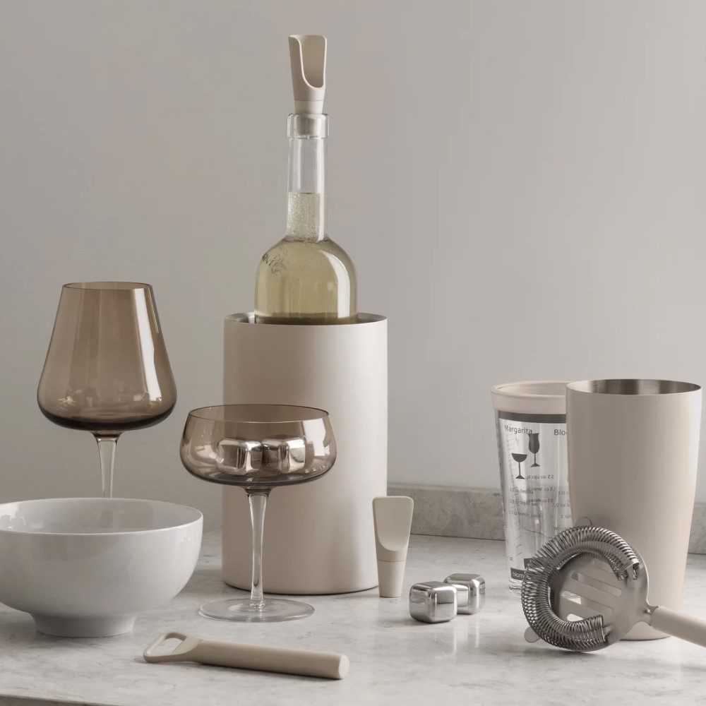 A table adorned with different shaped wine glasses, an ice bucket, and a cylinder-shaped wine cooler.