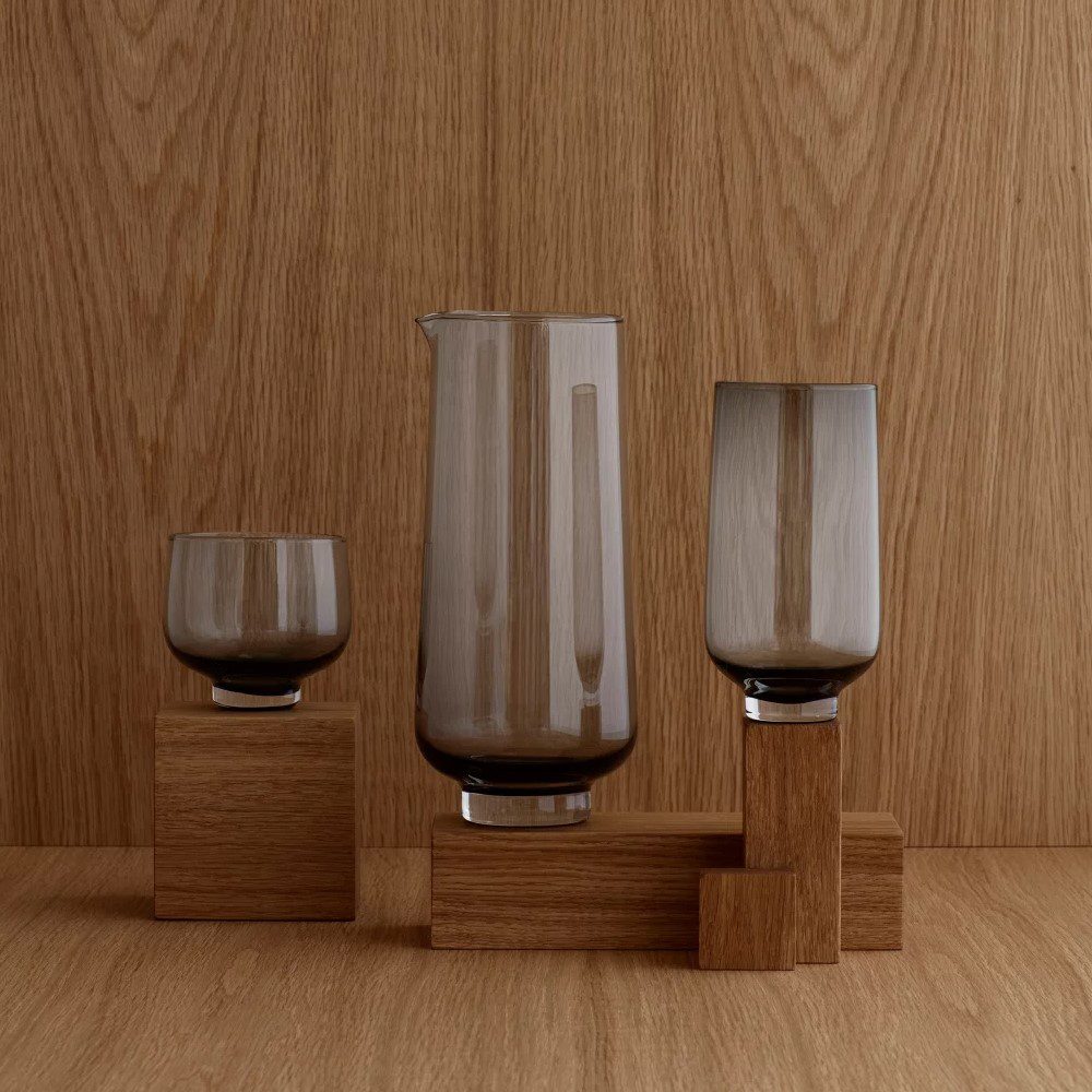 A cylindrical-shaped water jug in the middle placed next to a tall and short glass.