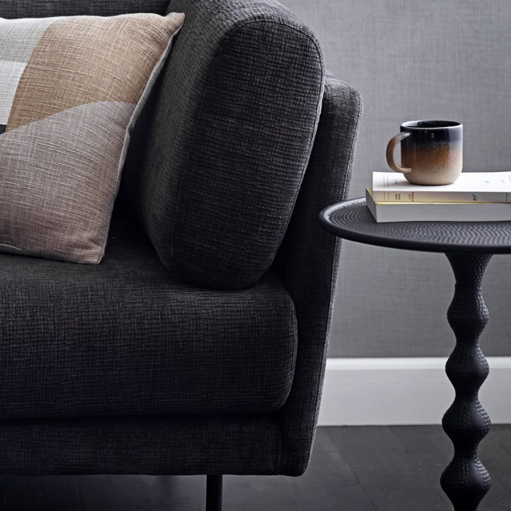 Cropped view of a sofa next to a side table with a book and a cup of coffee placed on top of the table.