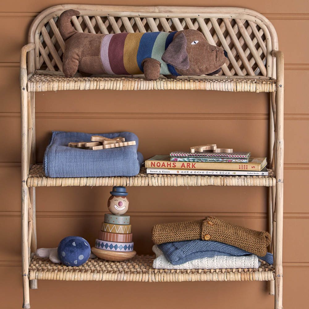 A packshot of Sigfred wooden stacking toy on a shelf with baby blankets and a soft plush toy dog.