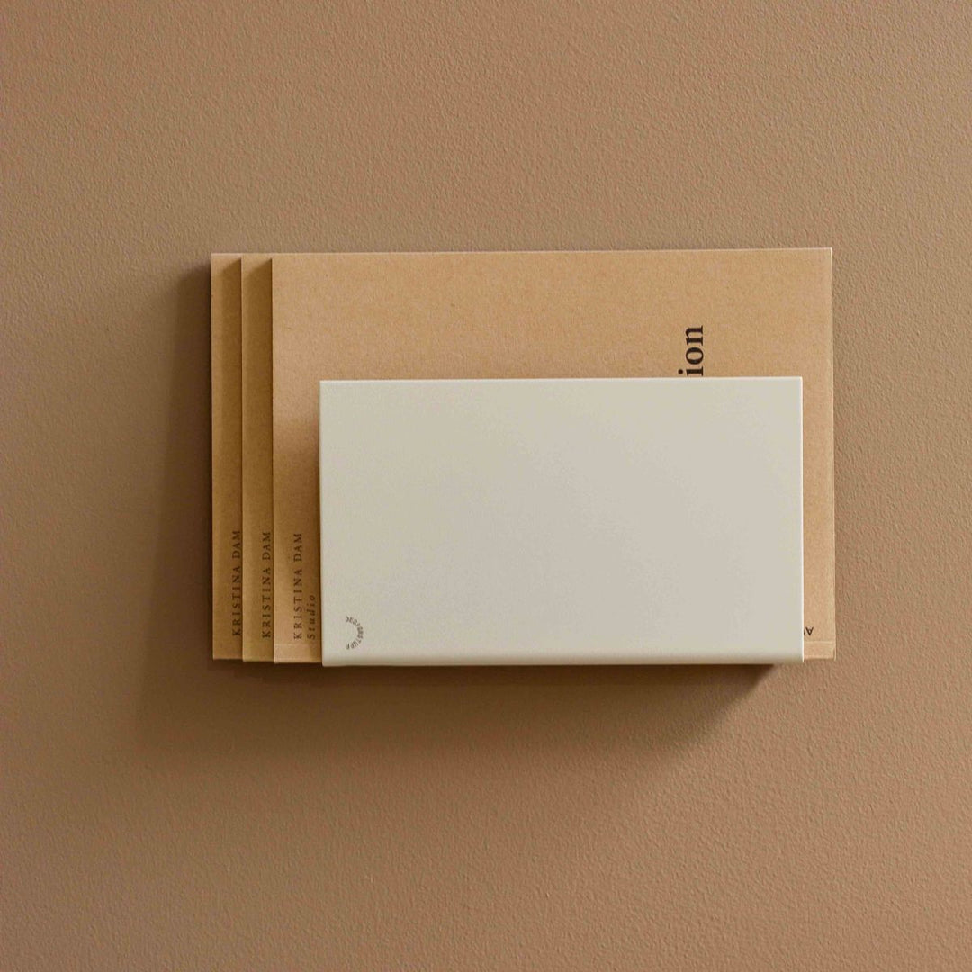 Natural light, perspective view of a beige, wall-mounted magazine holder.