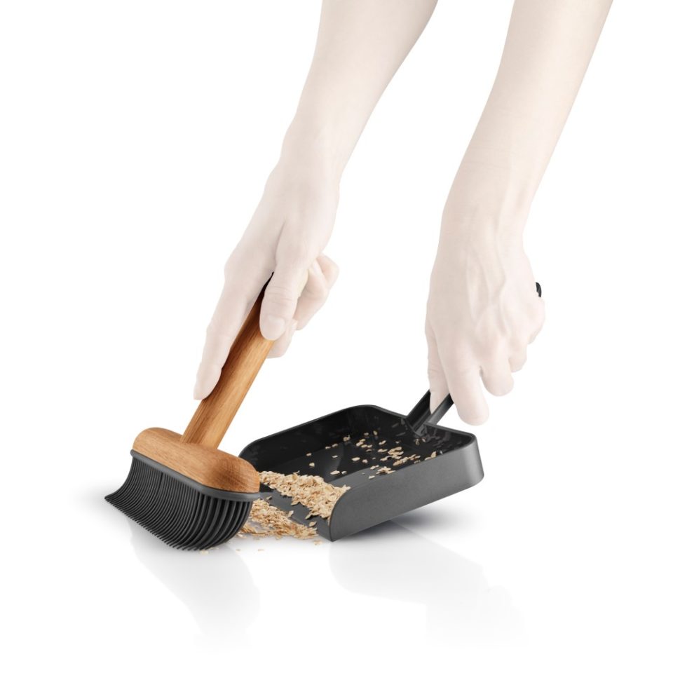 White background, studio lighting, cropped, perspective view of hands using a dustpan brush set sweeping oatmeal off the floor.