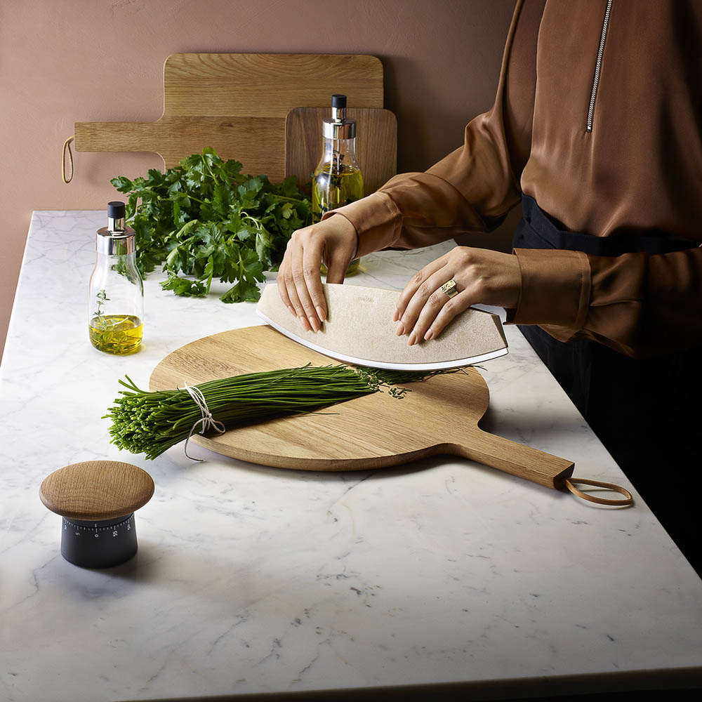 A woman is chopping the vegetable on a wooden board with kitchen timer on a marble bench.