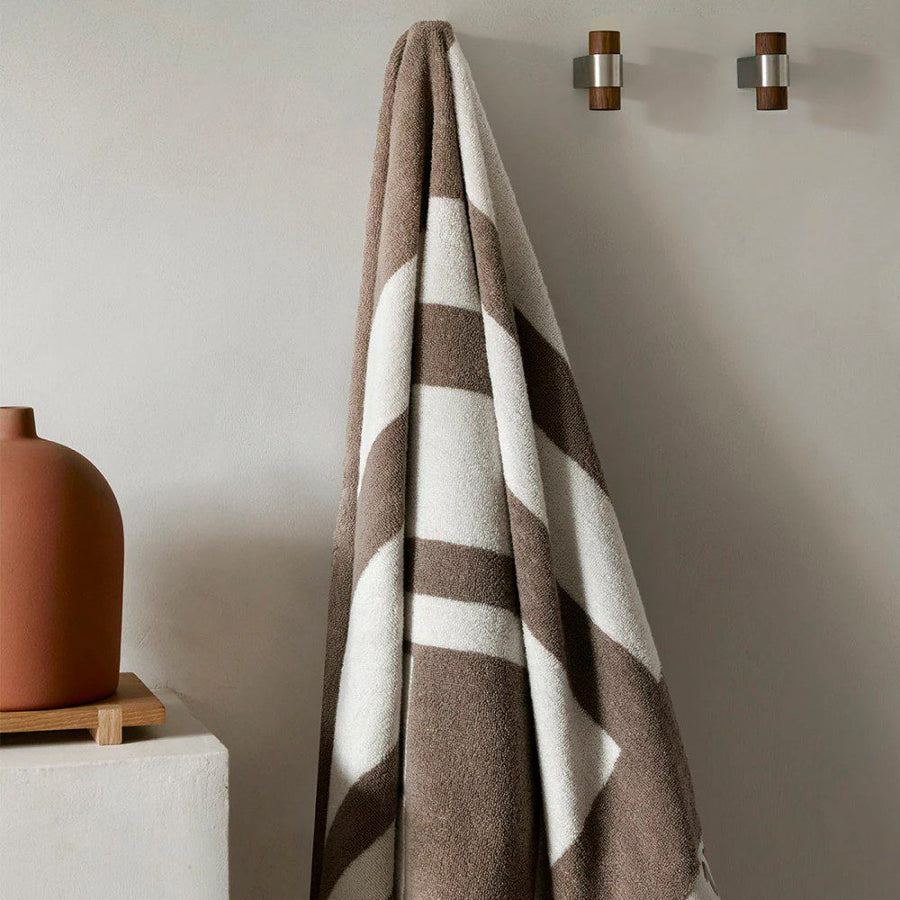 A large bathroom towel hung on a wooden dowel next to a jar.