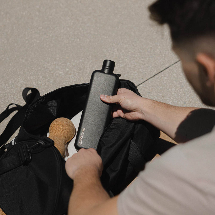 A person is pulling a Memobottle A5 stainless steel water bottle out off a bag