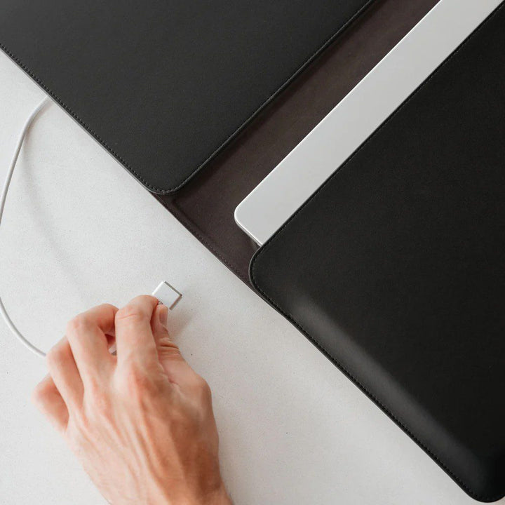 A person about to recharge their laptop computer tucked inside of a hybrid laptop sleeve and desk mat.