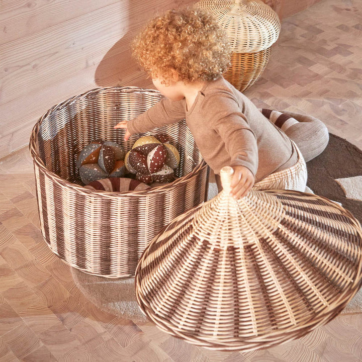 A kid is opening the lid of Circus rattan basket to grab the toys.