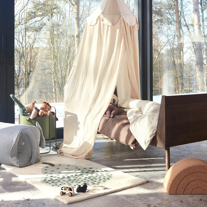 The modern kids room with tufted pear rug and a wooden bed with a white canopy.