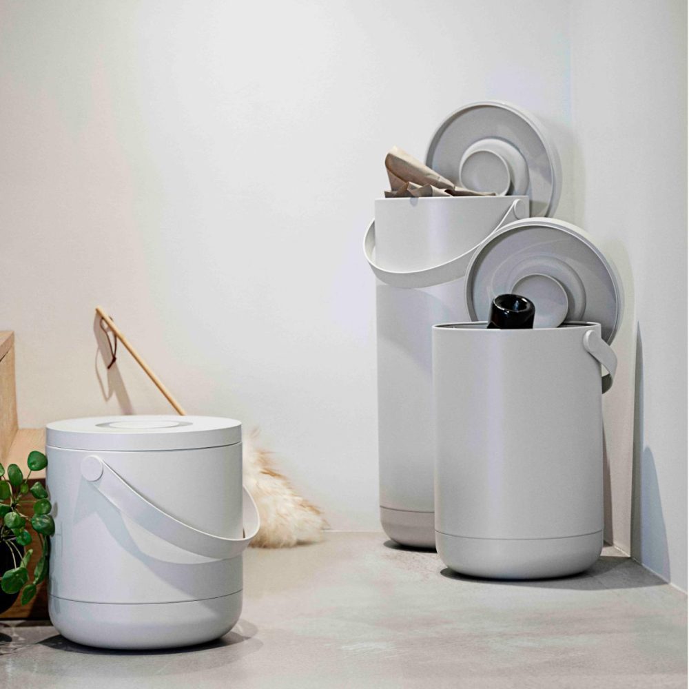 Natural light, perspective view of a grey, cylindrical laundry basket on the floor with towels placed on top of it.