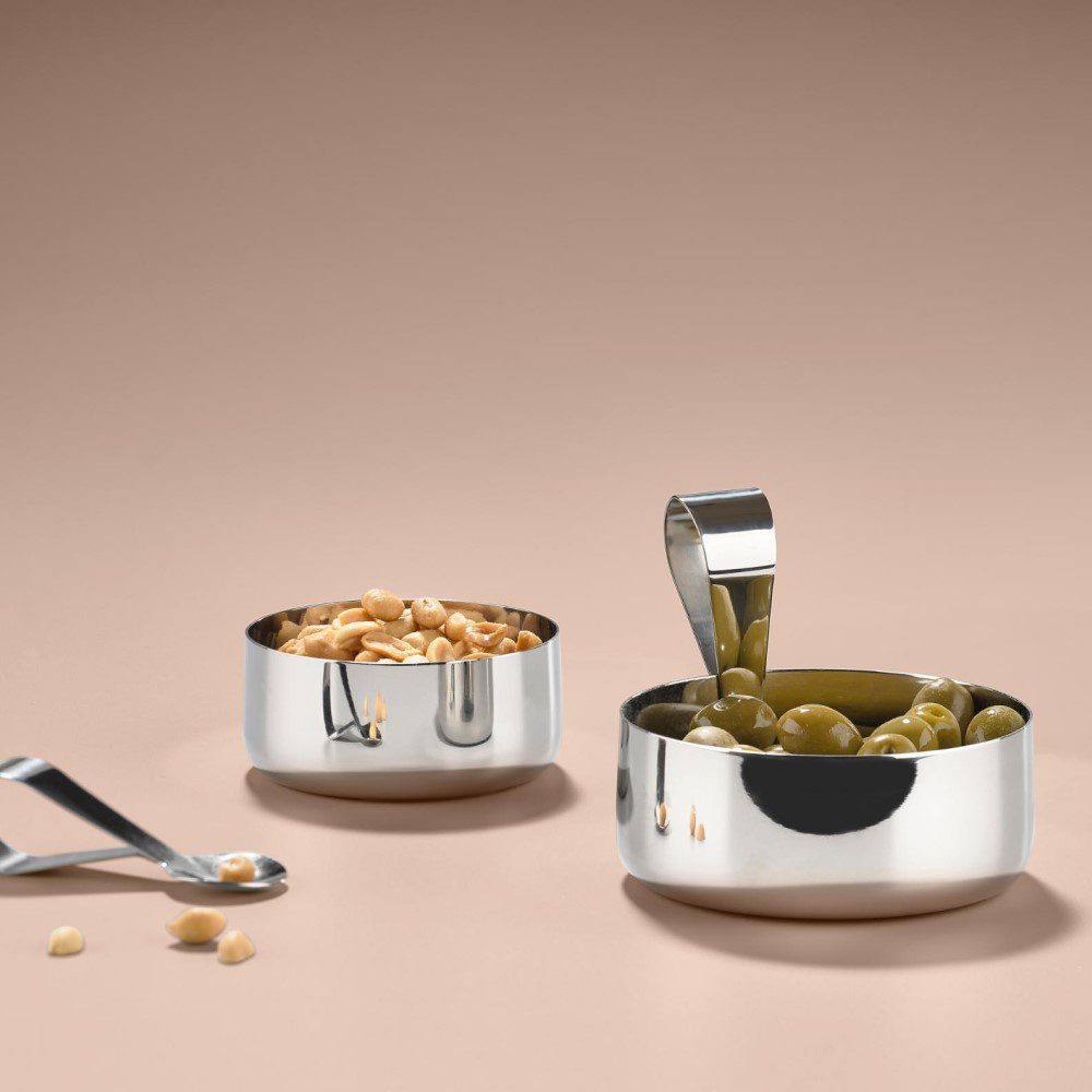 Studio image, perspective view of two filled silver-colored serving bowls with one spoon clipped on the rim and the other spoon outside of the serving bowl.