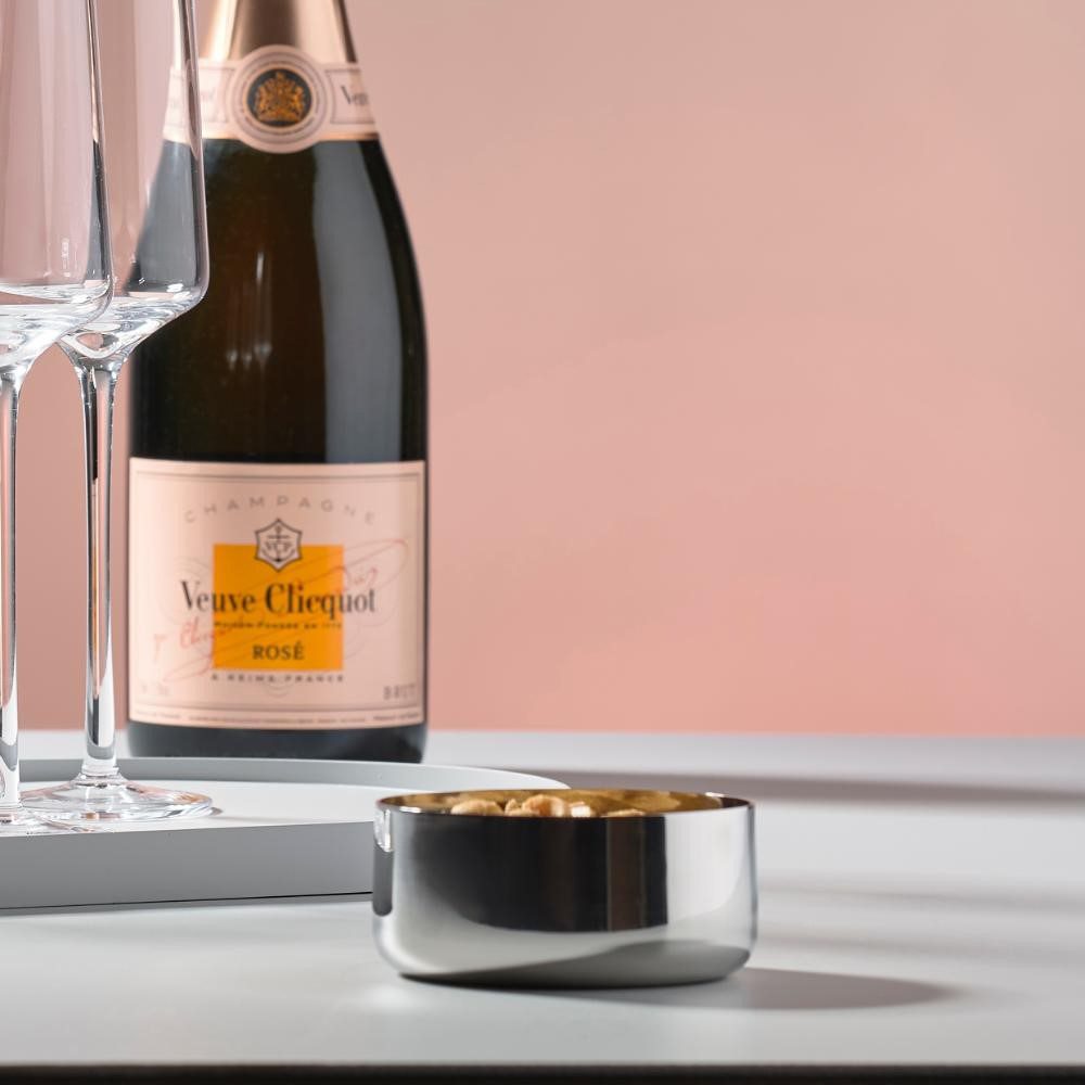 Studio image, perspective view of a filled silver-colored serving bowl in foreground with two champagne glasses and a bottle of champagne in the background.